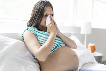 A pregnant woman posing while lying on a bed at home with tissuの写真素材