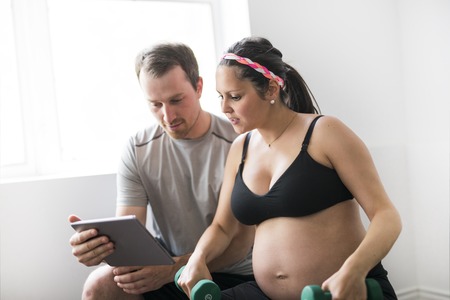 Pregnant woman working out with dumbbells with personal trainer at the gym