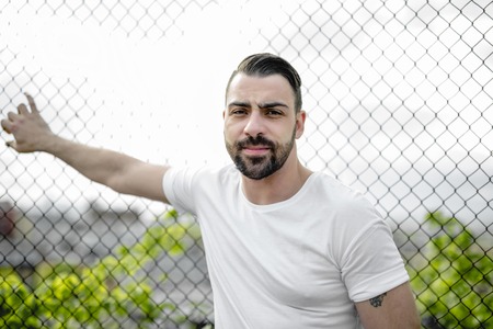 A pretty men standing near chain link fenceの写真素材