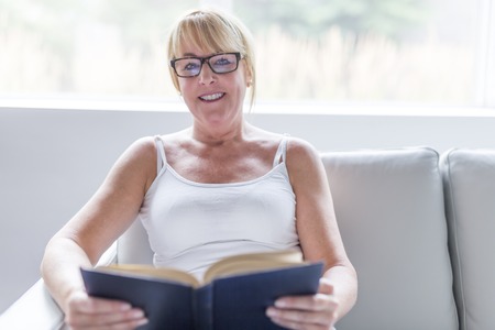 Shot of a mature woman reading her favorite novel while at home in living room.の写真素材