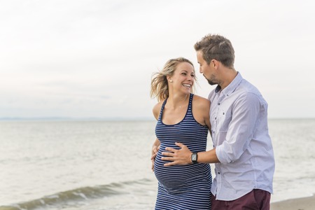 pregnant woman at beach with husband having funの写真素材