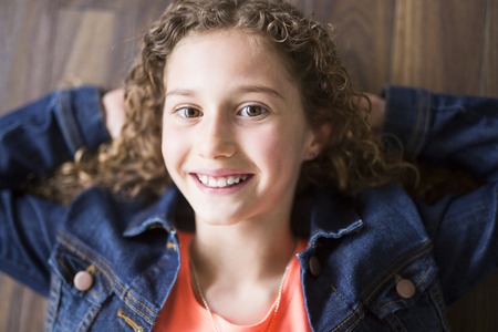 Smiling little girl stretched on a wooden floor with his hands behind his head and looking at cameraの写真素材