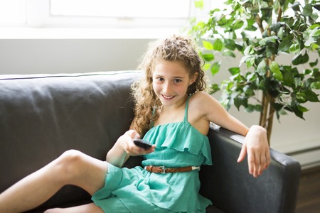 Young girl in living room with remote control smilingの写真素材