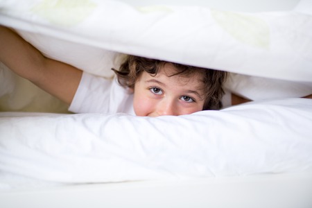 Adorable little boy in white t-shit lying in bedの写真素材