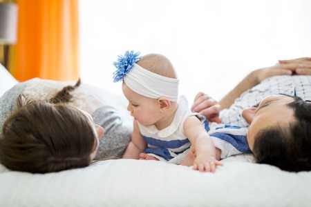 Happy family, mother, father and baby on the white bedの写真素材