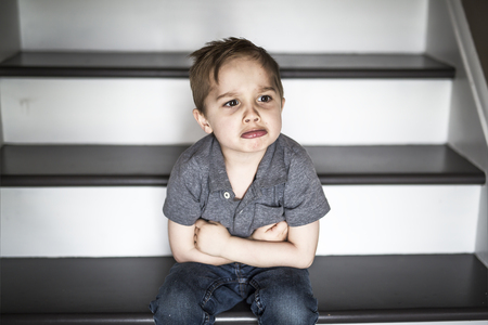one sad little boy sitting on the stairs in house at the day time.の写真素材