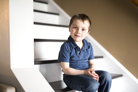 little boy sitting on the stairs in house at the day time.