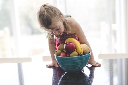Happy girl with a bowl of fruits at homeの写真素材