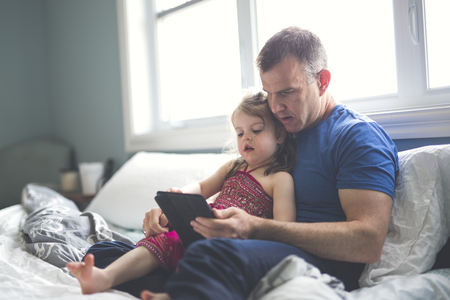 father and daughter relax in bed with tablet computerの写真素材