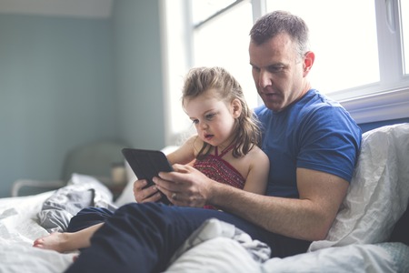 father and daughter relax in bed with tablet computerの写真素材