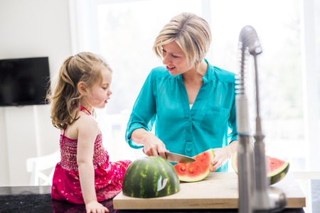 Mother and daughter cut watermelon in kitchenの写真素材