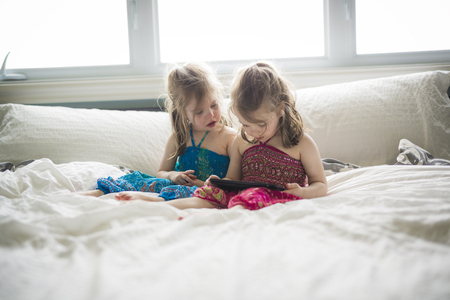 Closeup portrait of two girls lying on bed and using tabletの写真素材