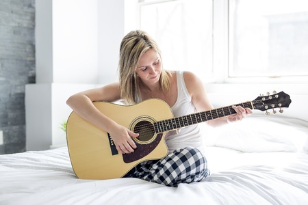 Smiling woman with guitar sitting on the bedの写真素材