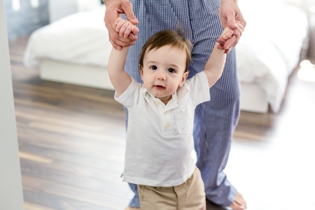 Father teaching a baby to walk in the bedroom at home