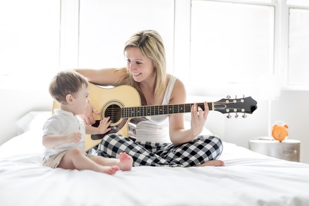 Smiling woman with guitar sitting on the bed with childの写真素材