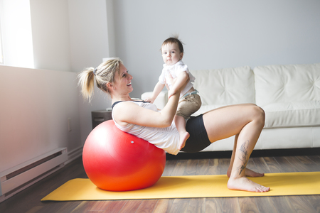 sports mother is engaged in fitness and yoga with a baby at homeの写真素材