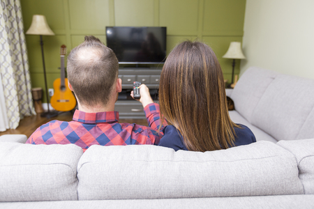 A Beautiful couple watching TV sitting on couch at homeの写真素材