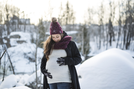 Young happy pregnant woman in snowy forestの写真素材