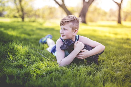 Cute, young boy in the garden holding a boxer dogの写真素材