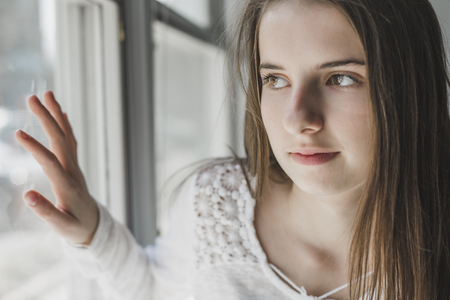 Beautiful young woman in front of a window looking outsideの写真素材
