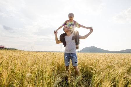young father with his little son walking in the wheat field at sunset in a warm summer dayの写真素材