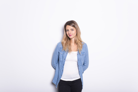 Young Woman in Denim Shirt and Jeans, Leaning Against Gray Wall Backgroundの写真素材