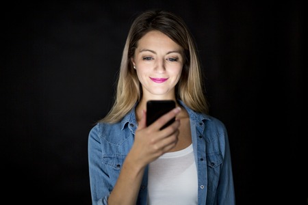 Closeup of woman holding and using modern smart phone on black background