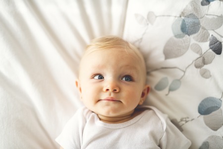 Cute baby girl lying on white sheet at home