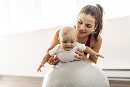 A Portrait of beautiful young mother in sports wear with her charming little baby in training sessionの写真素材