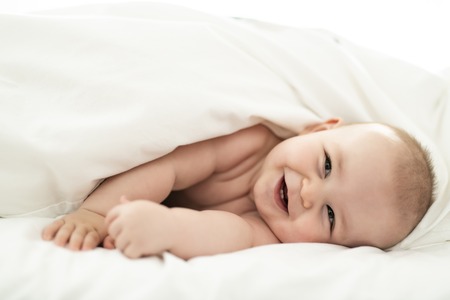 happy cute baby lying on white sheetの写真素材