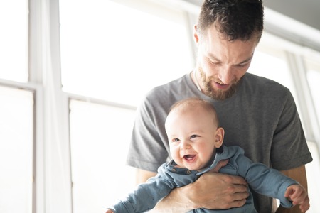 father holding his baby son in the arms close to a windowの写真素材
