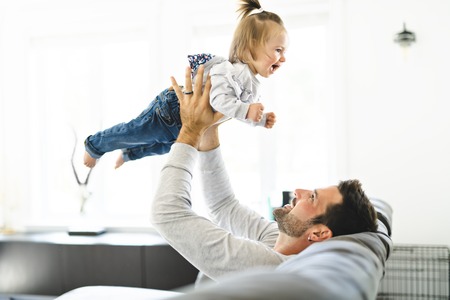 Young father with baby daughter on sofa at homeの写真素材