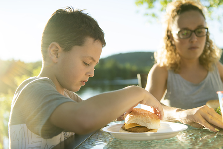 boy eating hamburger outside with his familyの写真素材