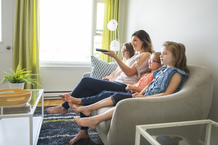 mother and daughters on sofa at home listening TV
