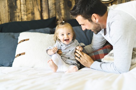 Father and his baby daughter on bed having fun