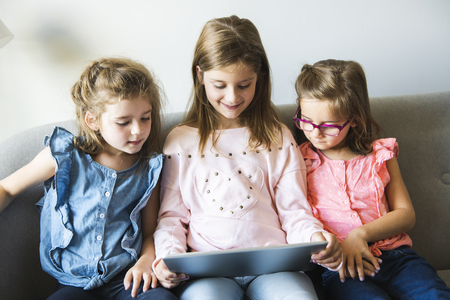 Three sisters girls sit on the sofa at home with tabletの写真素材