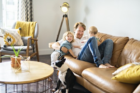 Young father with baby daughter and son on sofa at homeの写真素材