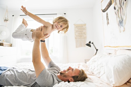 Happy father playing with his boy on a bed at homeの写真素材