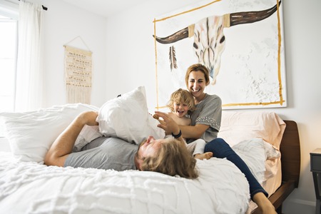 Family with child having fun on bed with pillow fightの写真素材