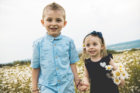 Two cute childs playing in green daisy field