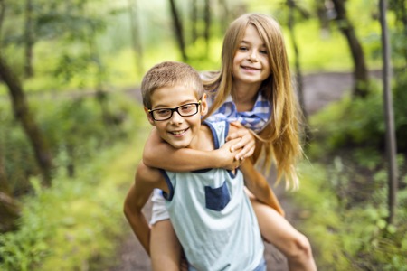 brother and sister giving piggyback in forestの写真素材