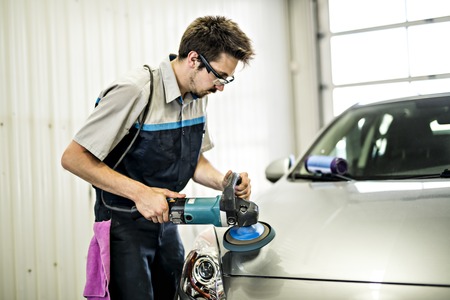 Man at work cleaning automobile at car wash waxy
