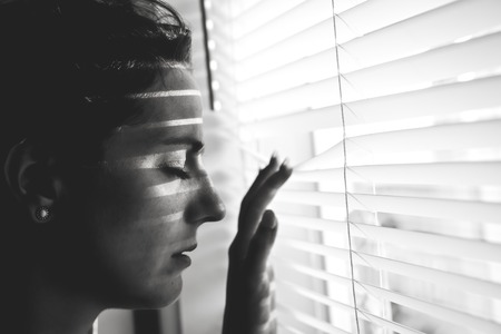 Depressed young woman near window at home, closeupの写真素材