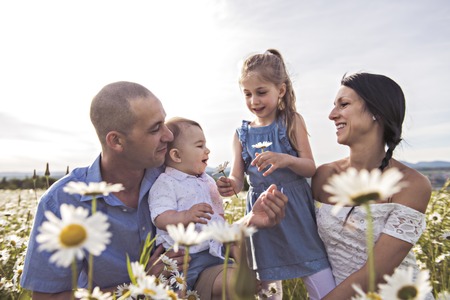 Happy family having fun on daisy field at sunset
