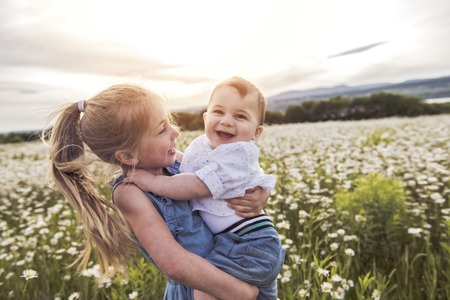 Cute child girl at camomile field daisy with baby brother