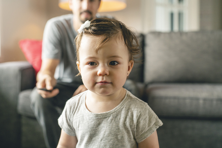 Happy young father on the sofa with tv remote and little daughterの写真素材