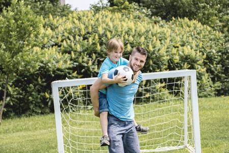 Man with child playing football outside on fieldの写真素材