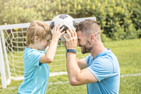 Man with child playing football outside on fieldの写真素材