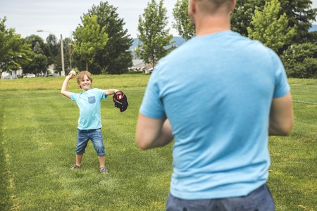 Handsome dad with his little cute sun are playing baseball on green grassy lawnの写真素材