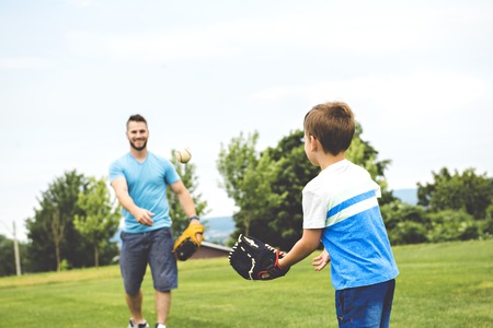 Handsome dad with his little cute sun are playing baseball on green grassy lawnの写真素材